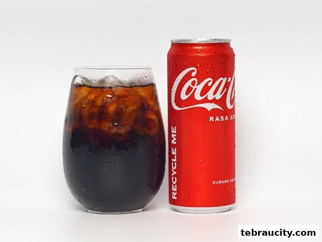 A refreshing glass of Coca-Cola with ice next to a cold can of Coca-Cola.