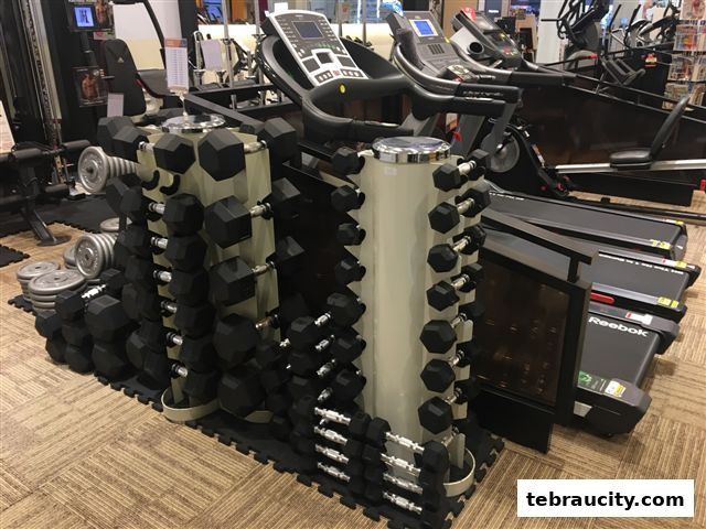 A display of dumbbells and weight plates, with treadmills in the background.