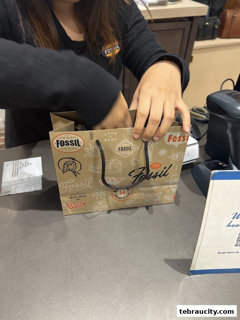 A person is placing items into a Fossil branded shopping bag at a counter.