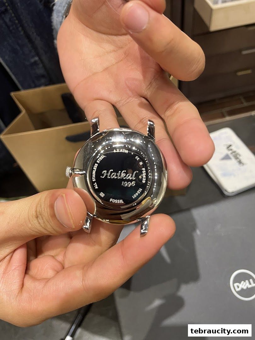 Hands holding the back of a Fossil watch with 'Haikal 1996' engraved.