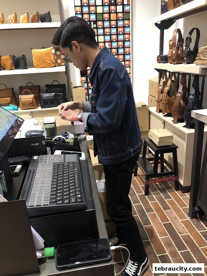 A person stands at a counter in a shop filled with bags and accessories.