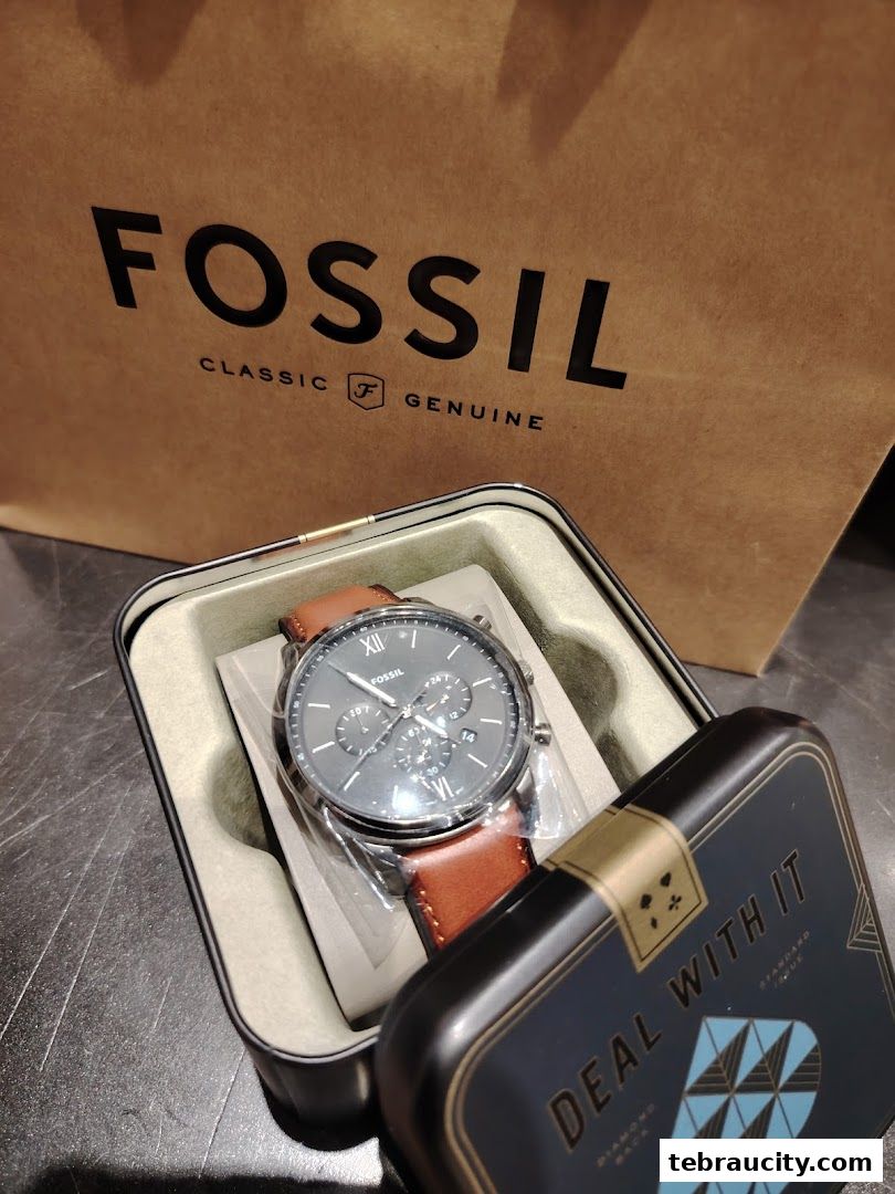 A Fossil watch in its tin packaging with a shopping bag in the background.