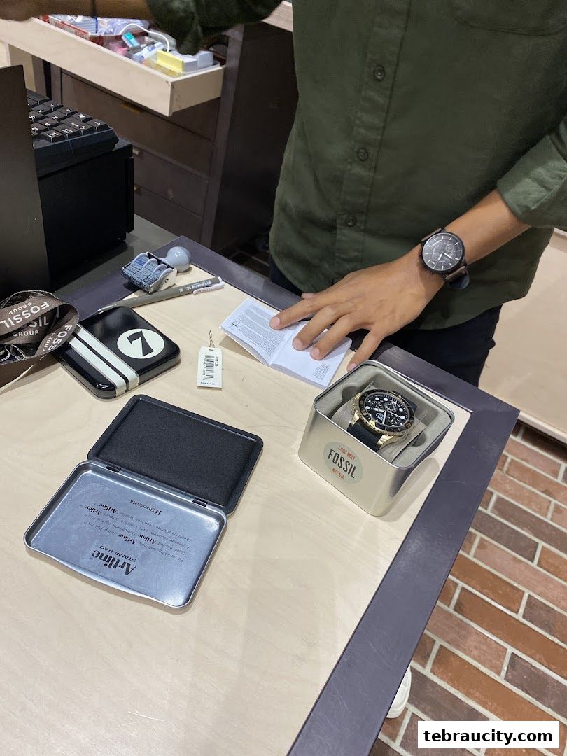 A Fossil watch is displayed in its box next to a stamp pad and other accessories.