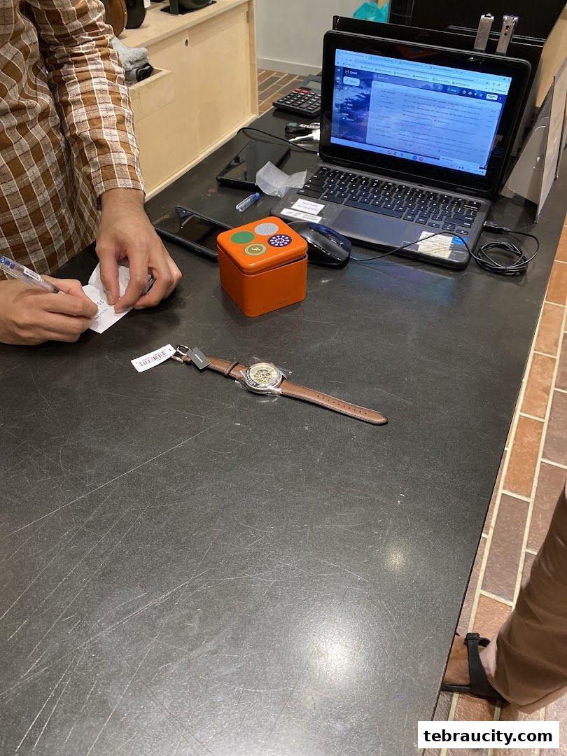 A person is writing on a receipt at a counter with a watch and a Fossil tin.