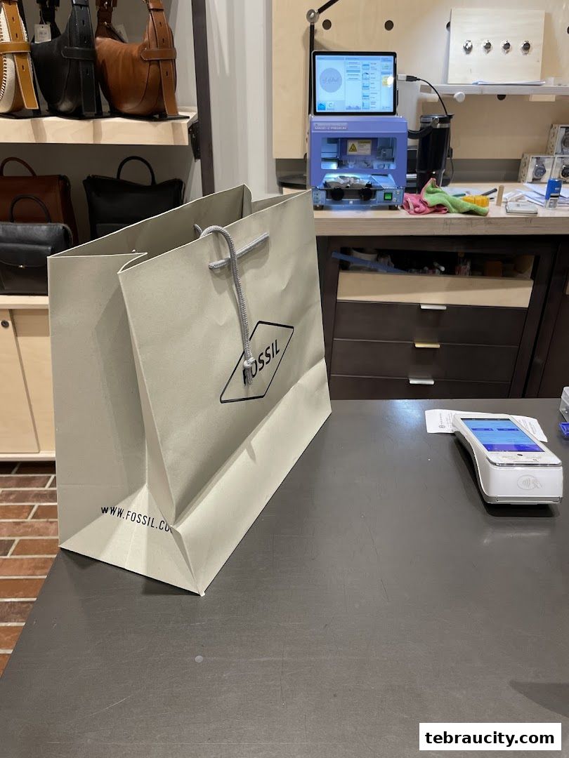 A Fossil shopping bag sits on a counter next to a payment terminal and watch repair equipment.