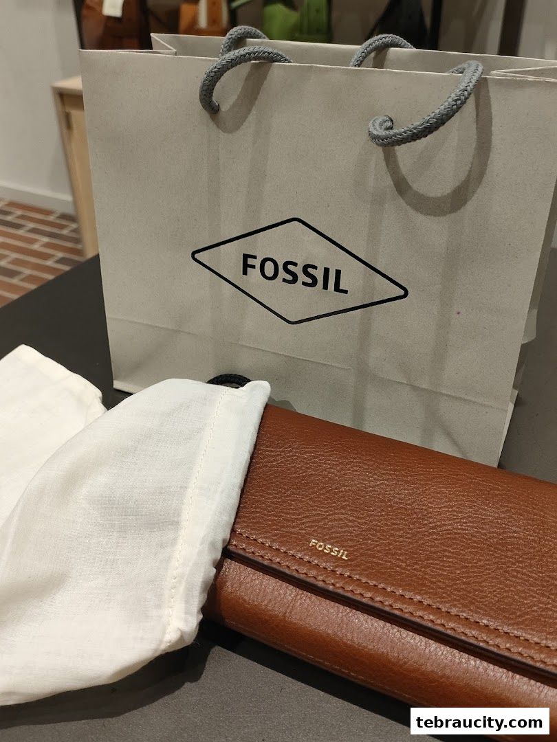 A brown leather Fossil wallet and a Fossil shopping bag are displayed.