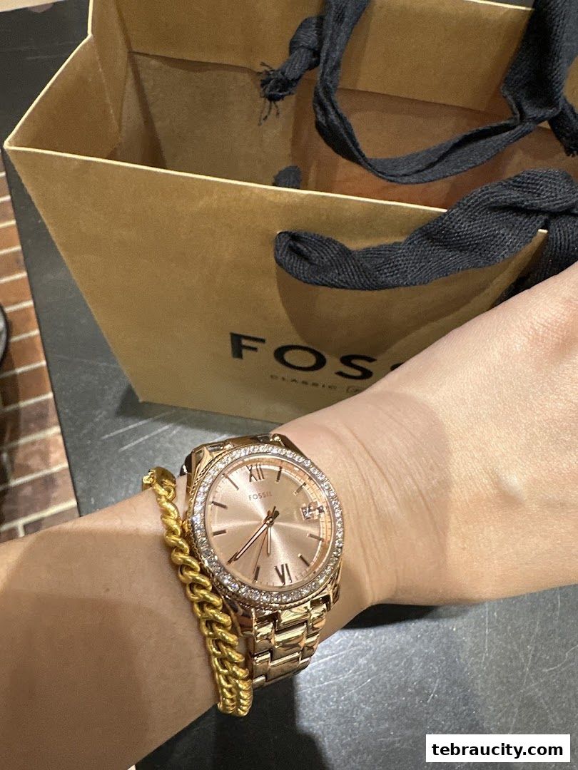 A person wearing a rose gold Fossil watch and bracelet with a Fossil shopping bag.