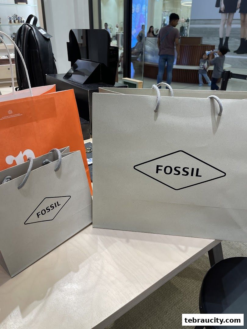 Fossil shopping bags displayed on a wooden surface with a store interior in the background.