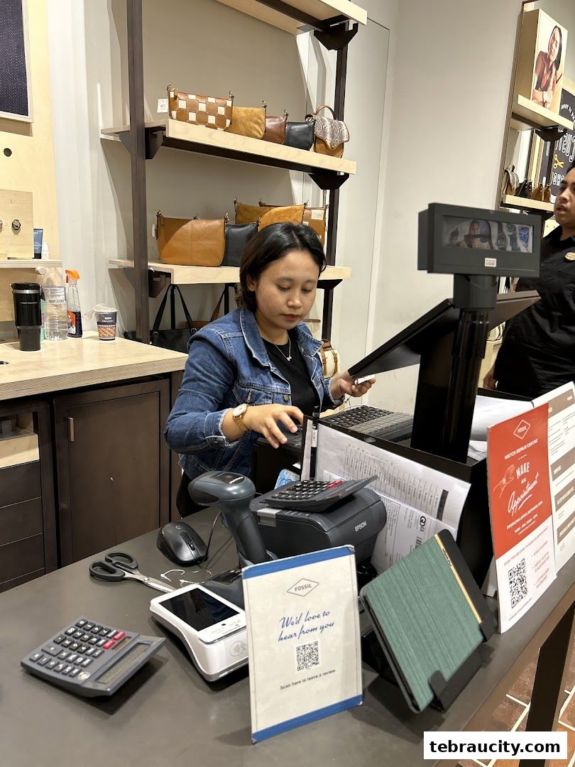 A cashier at Fossil Aeon Tebrau City is serving a customer at the counter.
