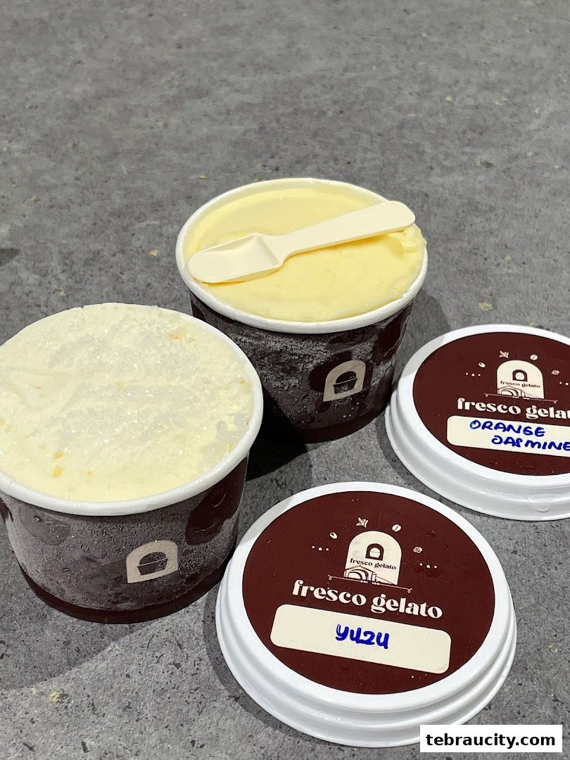 Two cups of gelato with spoons and two lids labeled with flavors.