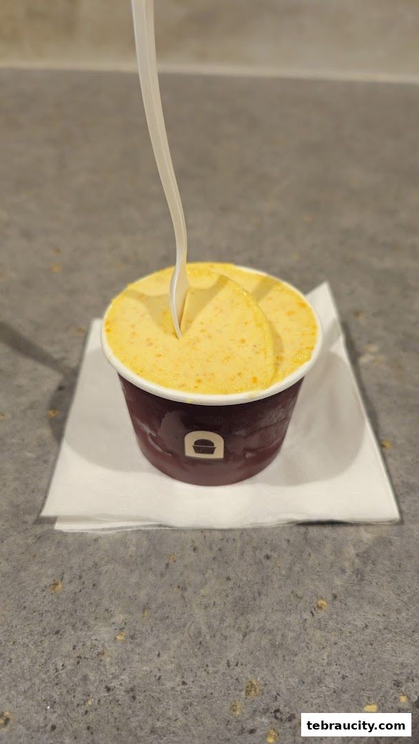 A cup of creamy yellow gelato with a spoon inserted, on a white napkin.