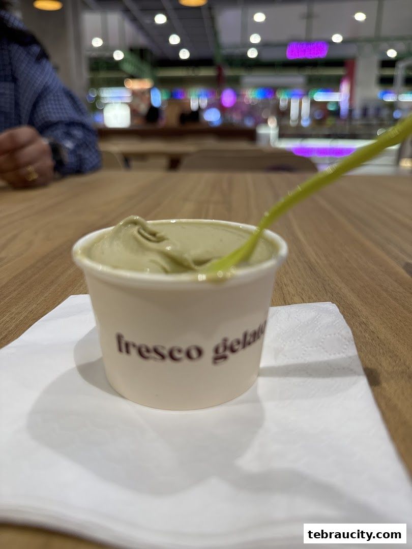 A cup of green gelato with a yellow spoon on a white napkin on a wooden table.