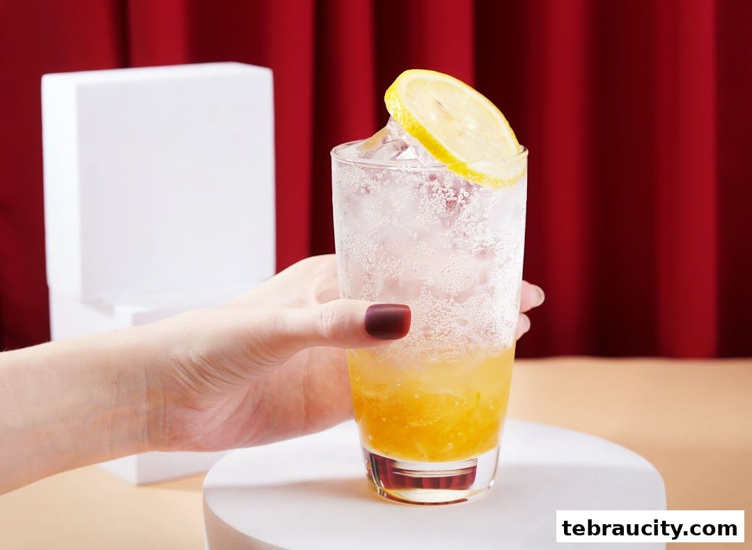 A hand holding a refreshing glass of iced beverage with lemon and bubbles.