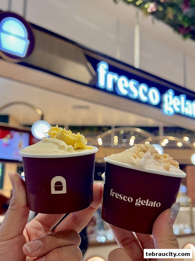 Hands holding two cups of gelato with the Fresco Gelato sign in the background.