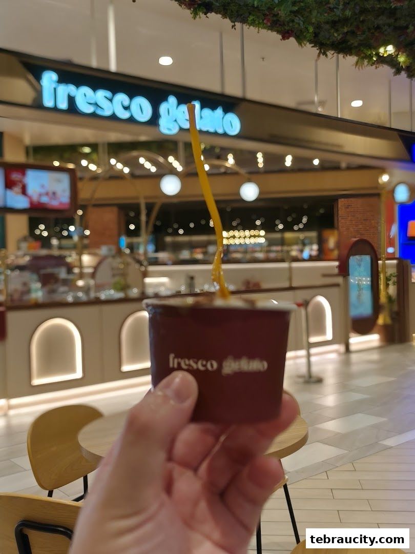 A hand holds a cup of gelato in front of the Fresco Gelato shop.