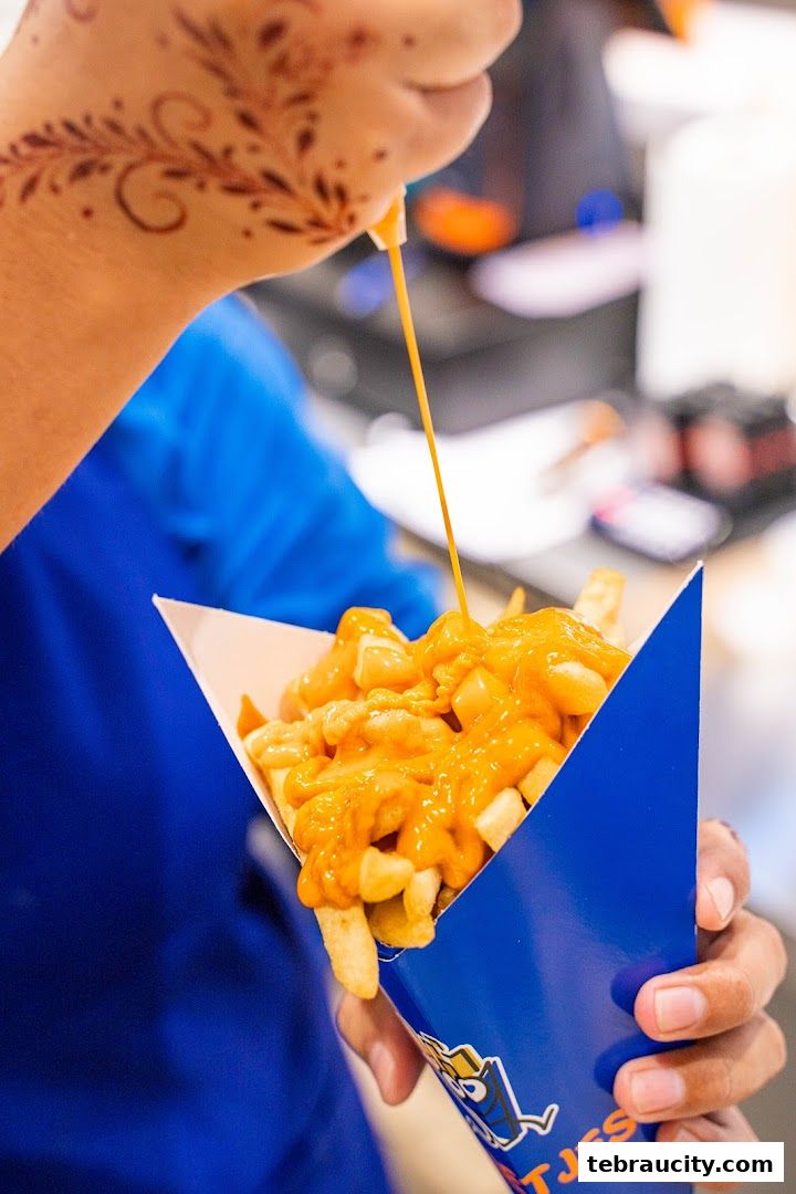 A person is drizzling cheese sauce over a cone of fries.
