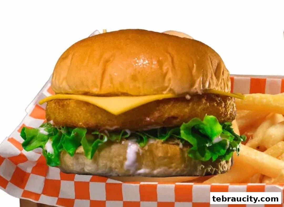 A close-up shot of a delicious fish burger with cheese, lettuce, and fries.