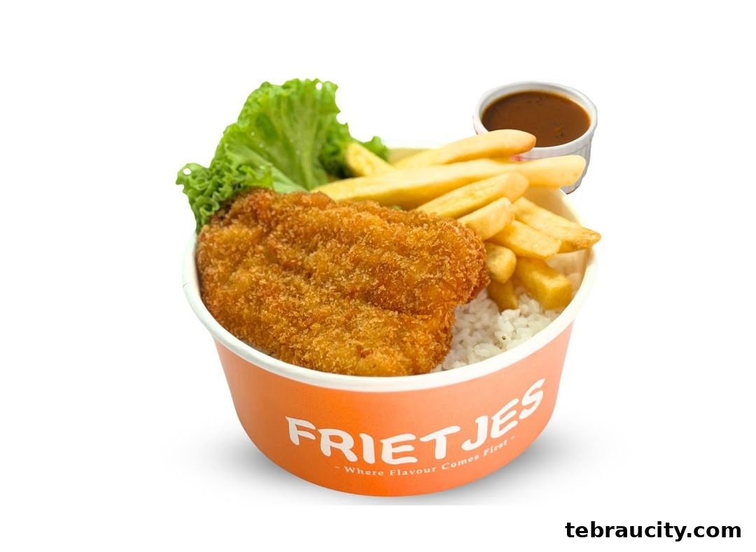 A bowl of rice topped with crispy fried chicken, french fries, lettuce, and a side of sauce.