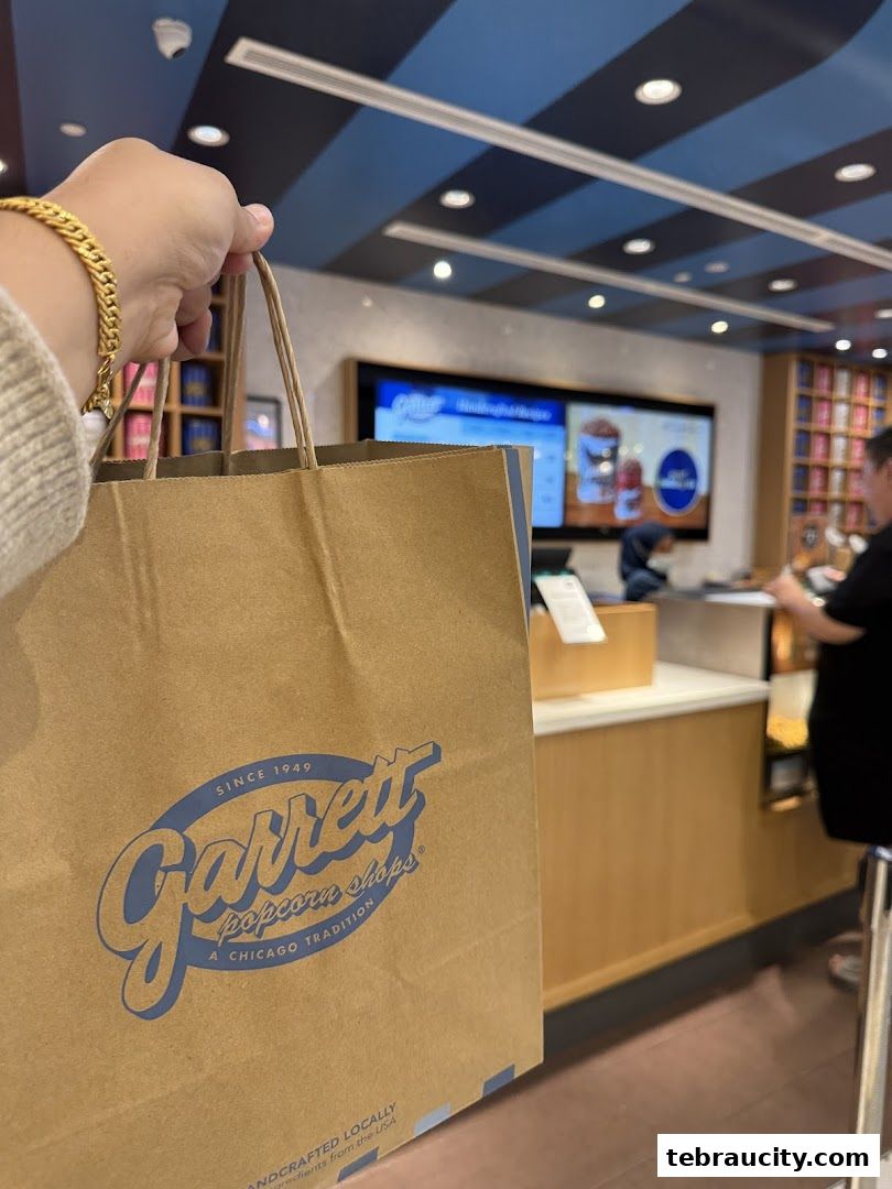 A hand holds a Garrett Popcorn Shops paper bag in front of the store counter.