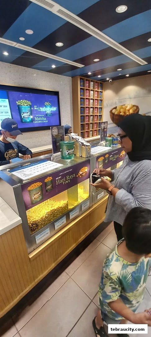 Customers ordering popcorn at a Garrett Popcorn Shops counter with various flavors displayed.