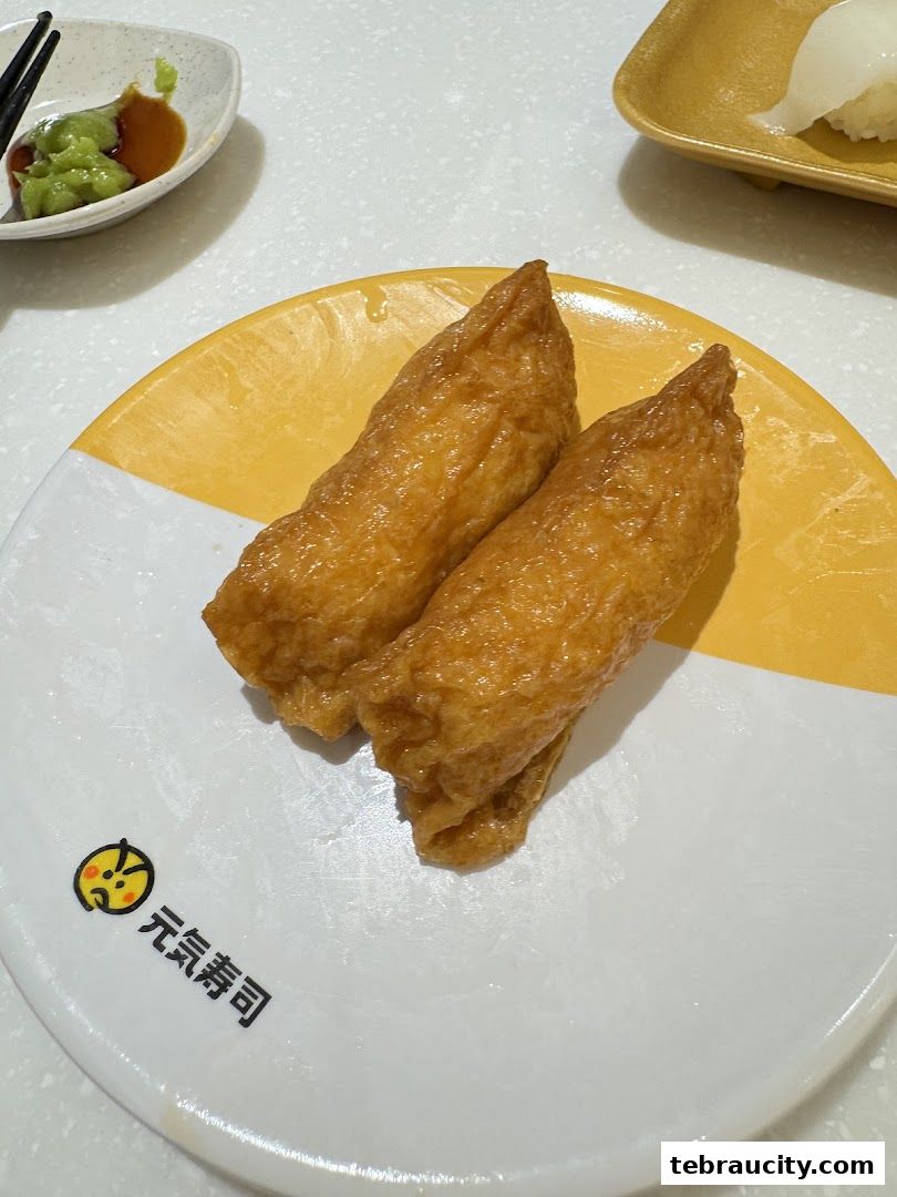 Two pieces of Inari sushi on a plate with wasabi and soy sauce in the background.