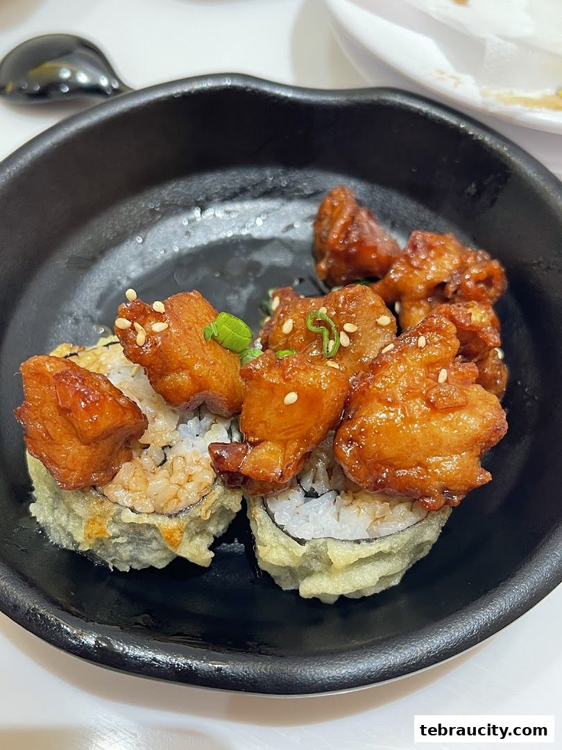 A close-up shot of a black bowl filled with sushi rolls topped with glazed fried chicken pieces.
