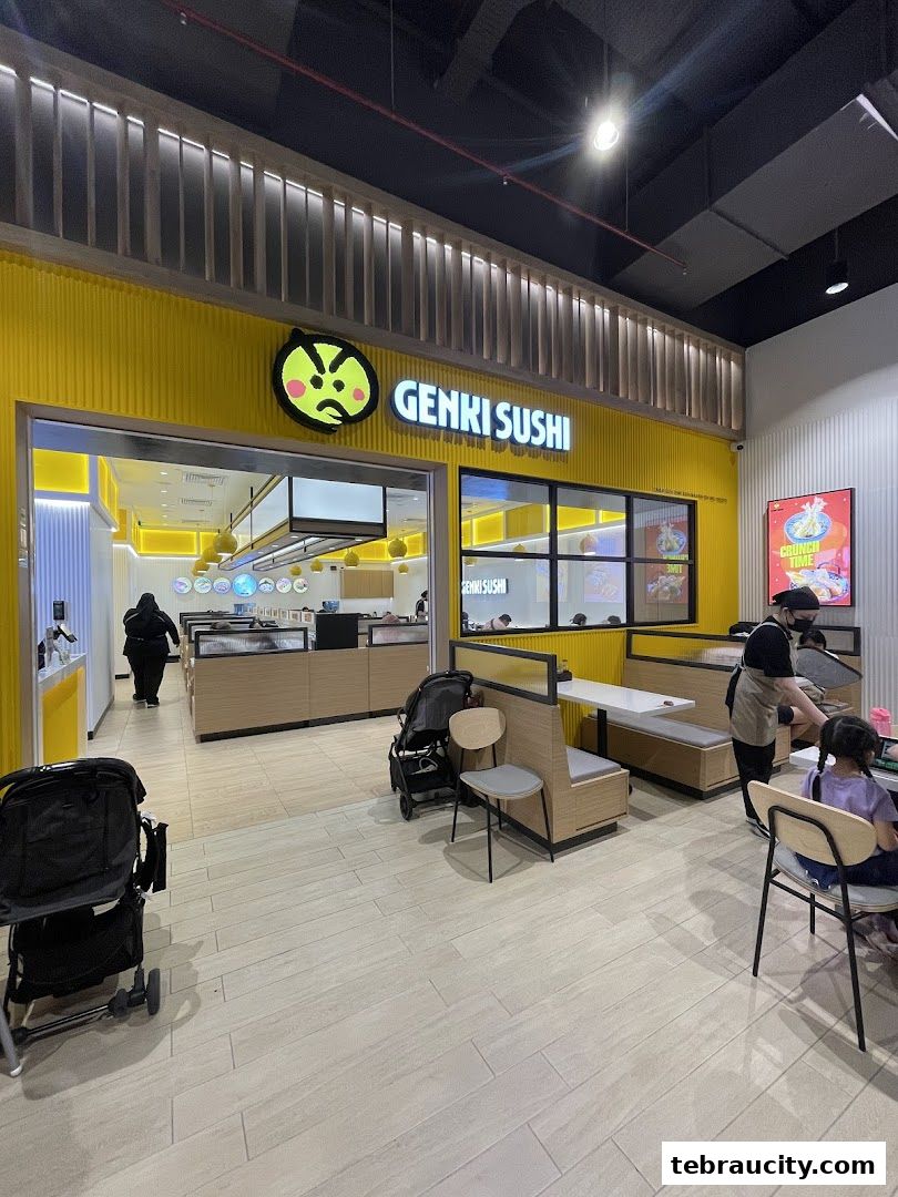 The bright yellow exterior of Genki Sushi with its distinctive logo and seating area visible.