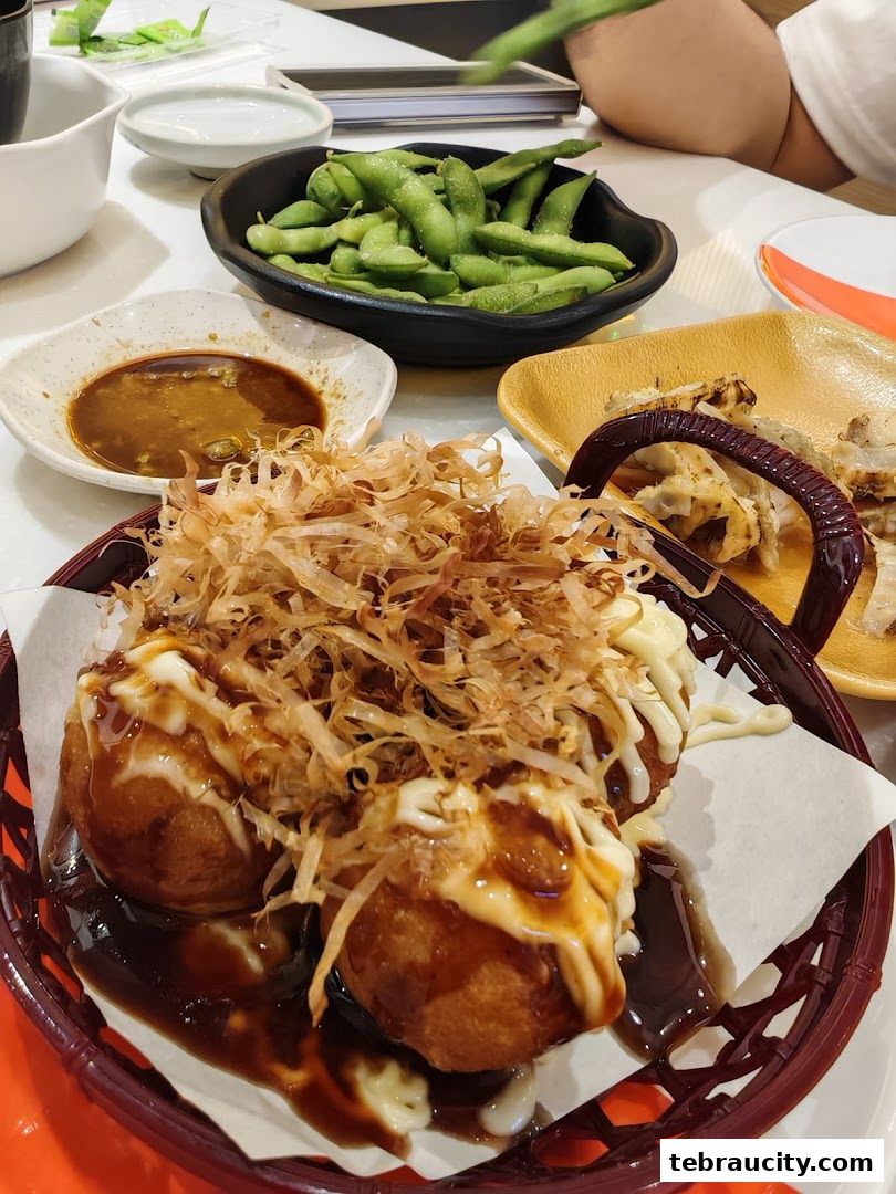 A close-up shot of delicious Takoyaki, edamame, and dipping sauce on a table.