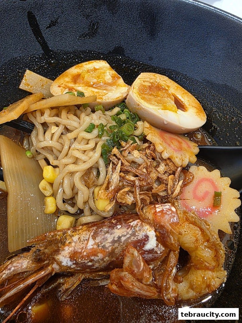 A close-up shot of a delicious ramen bowl with a large prawn, egg, noodles, and other toppings.