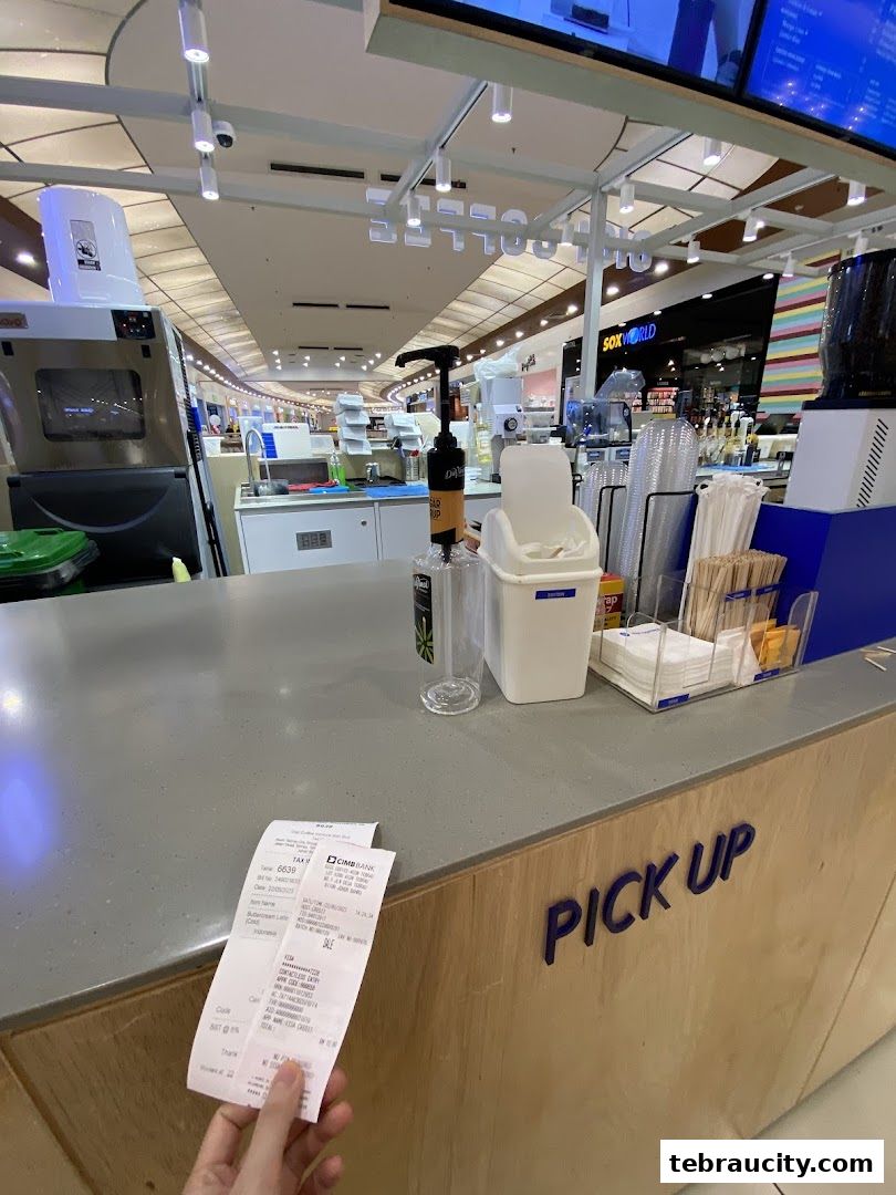 A receipt is held up at a coffee shop counter with a 'PICK UP' sign.