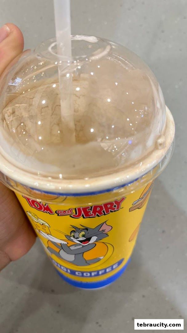 A hand holds a Tom and Jerry themed coffee cup with a straw.