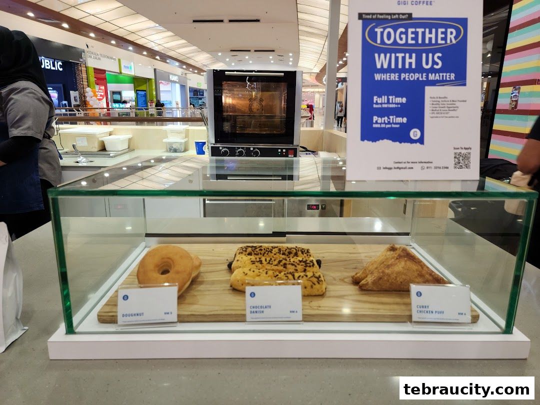 A display case with three pastries and a sign for Gigi Coffee in a mall.