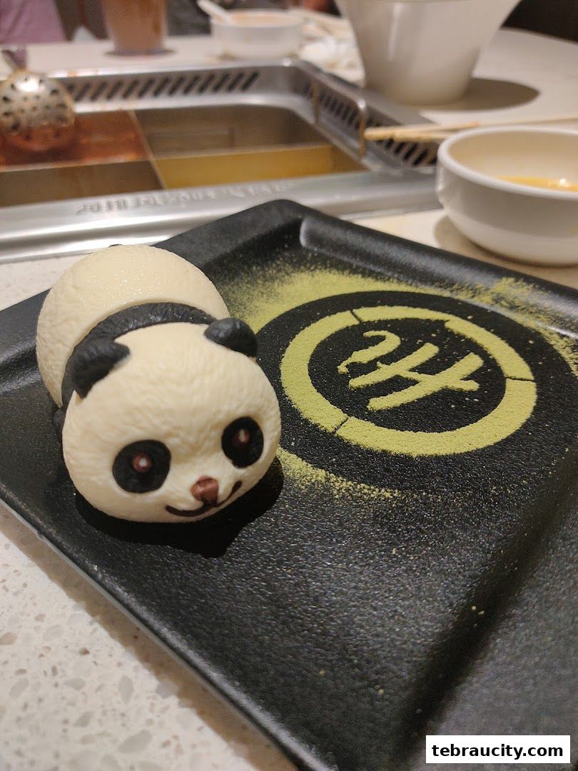 A cute panda-shaped dessert is presented on a black plate with green powder.