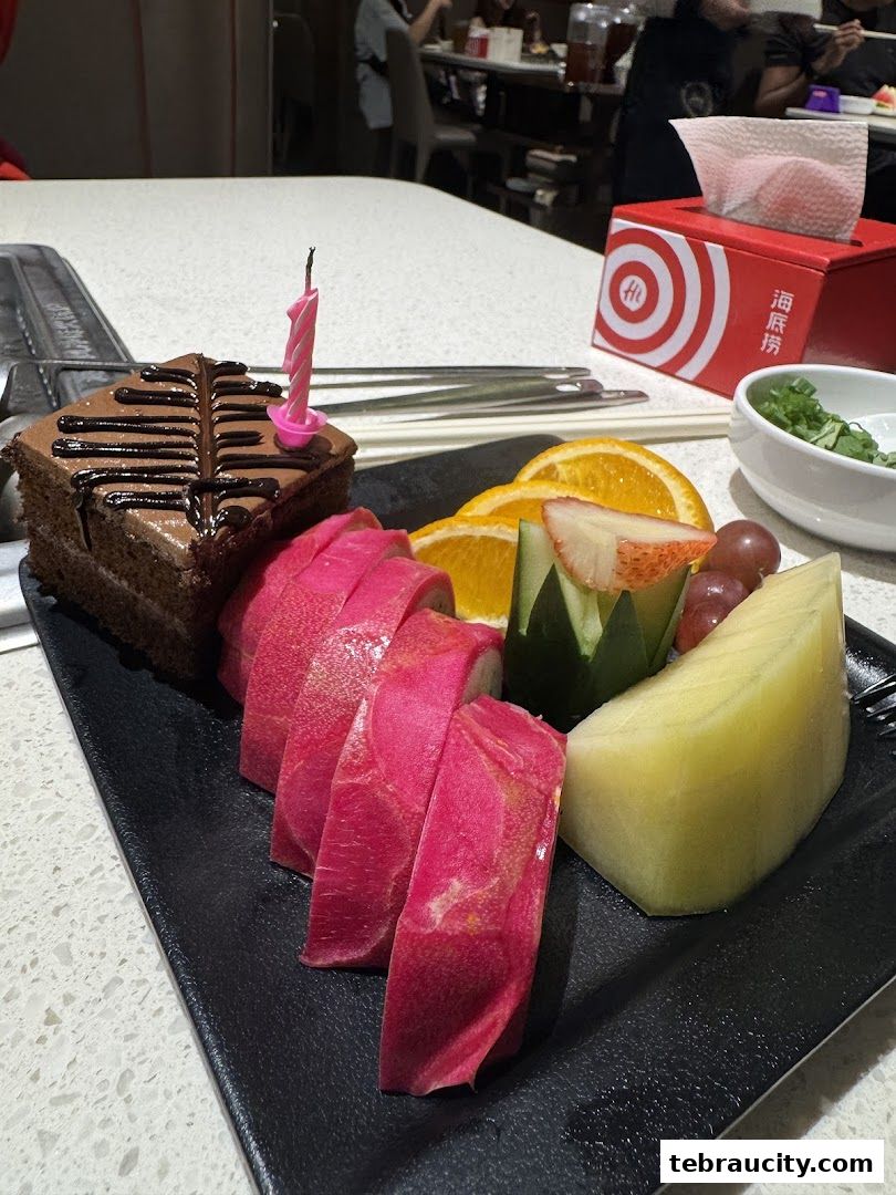 A slice of chocolate cake with a birthday candle, served with fruit and pickled radish.