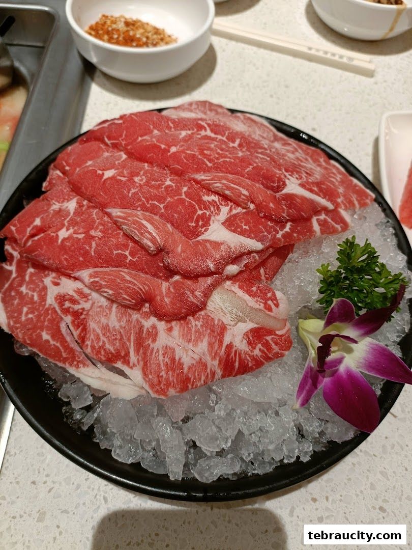 A plate of thinly sliced raw beef on ice, garnished with a flower and parsley, at a hot pot restaurant.
