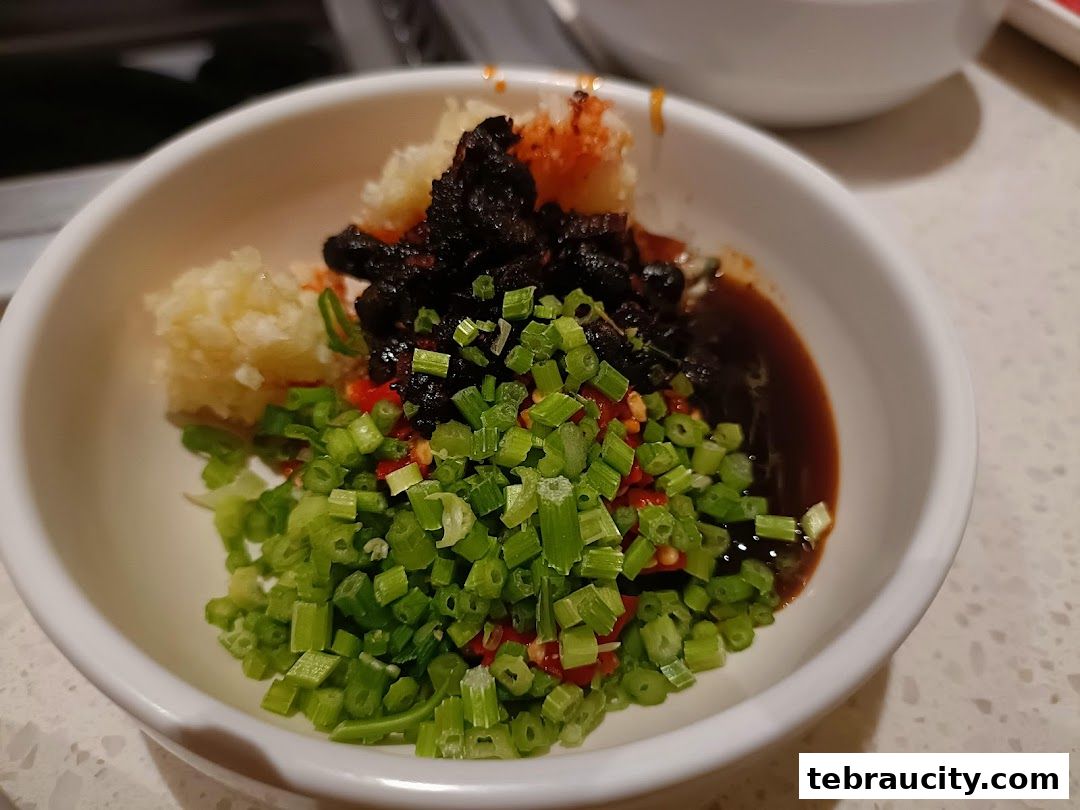 A close-up of a bowl filled with chopped scallions, chili, garlic, and a dark sauce.