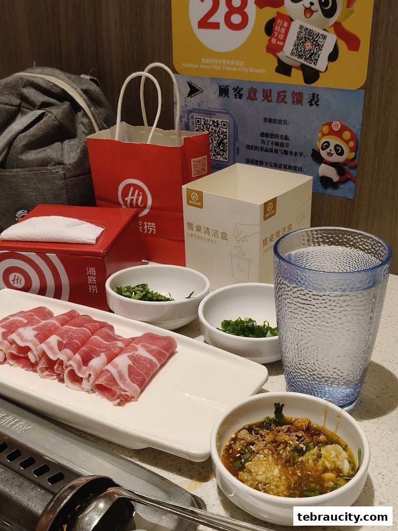 A table setting at Haidilao Hot Pot with thinly sliced meat, dipping sauce, and condiments.