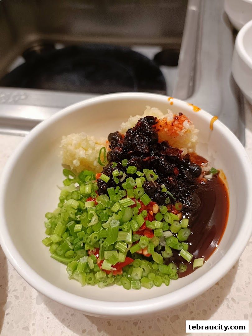 A bowl of chopped scallions, chili, garlic, and a dark sauce, ready for hot pot.