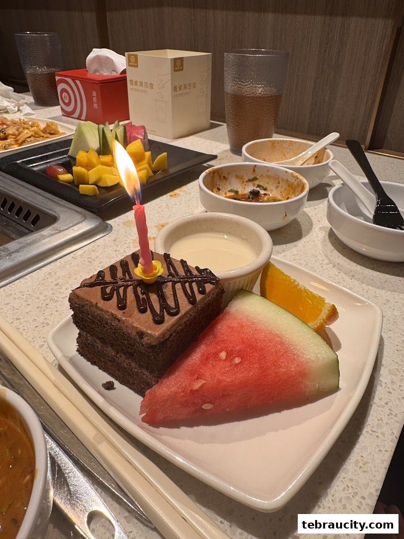 A slice of chocolate cake with a birthday candle, watermelon, and fruit on a table at Haidilao.