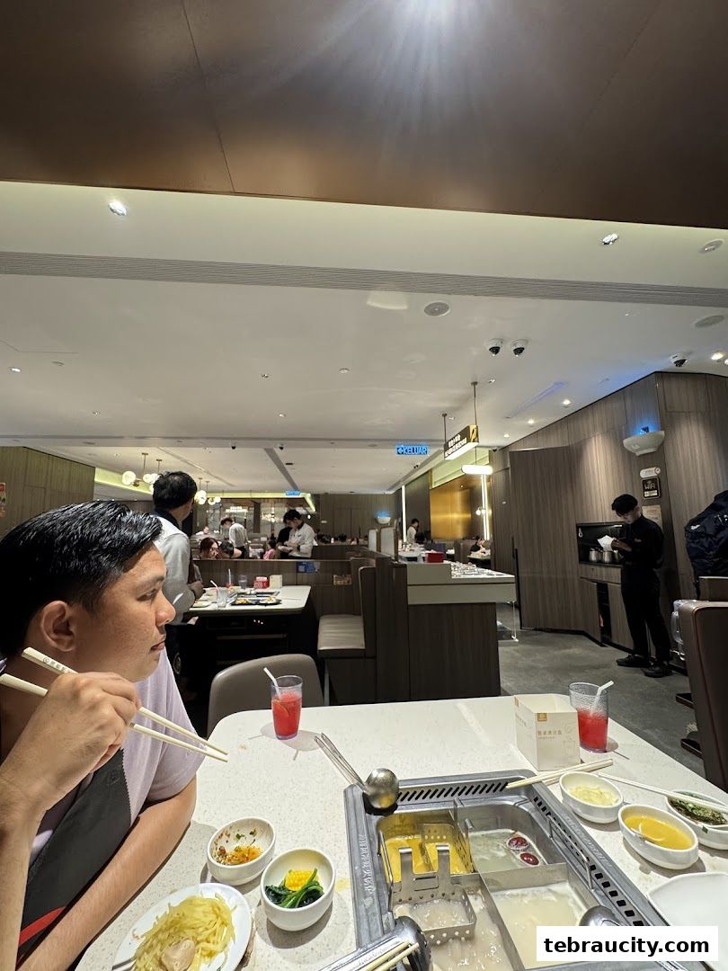 Diners enjoy hot pot at Haidilao, with a person in the foreground holding chopsticks.