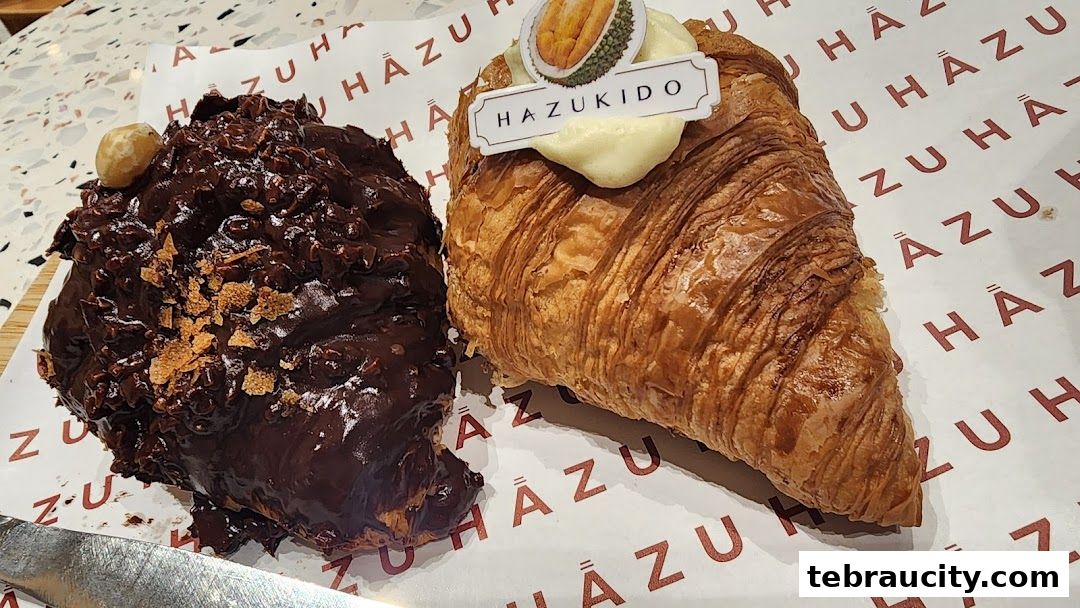 Two delicious pastries, one chocolate-covered and the other a croissant with durian topping, are displayed on branded paper.