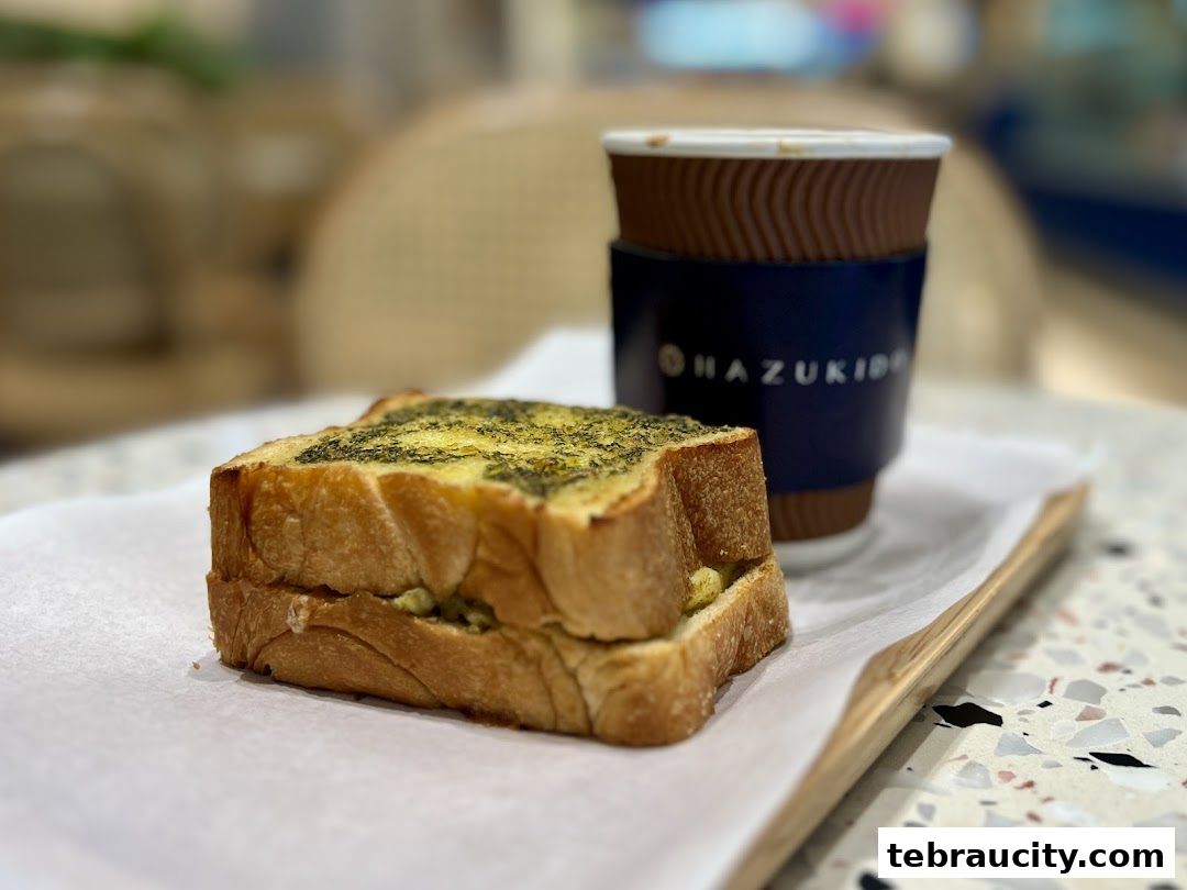 A close-up of a sandwich and a coffee cup with the Hazu Bakery Cafe logo.