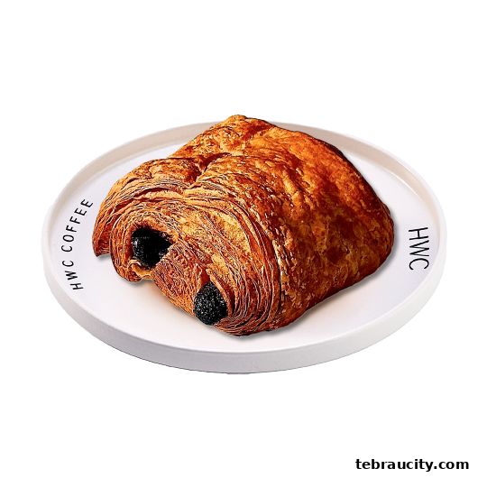 A flaky chocolate croissant on a white plate with HWC Coffee branding.