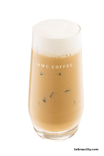 A tall glass of iced coffee with a creamy foam topping, branded with HWC Coffee.