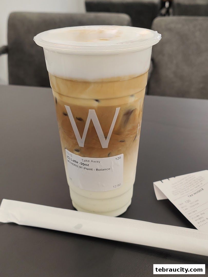 A tall iced latte with foam and a straw on a table.