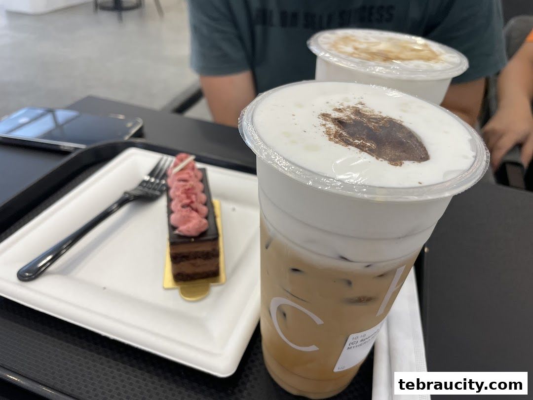 A chocolate cake with pink frosting and two iced coffees on a table.
