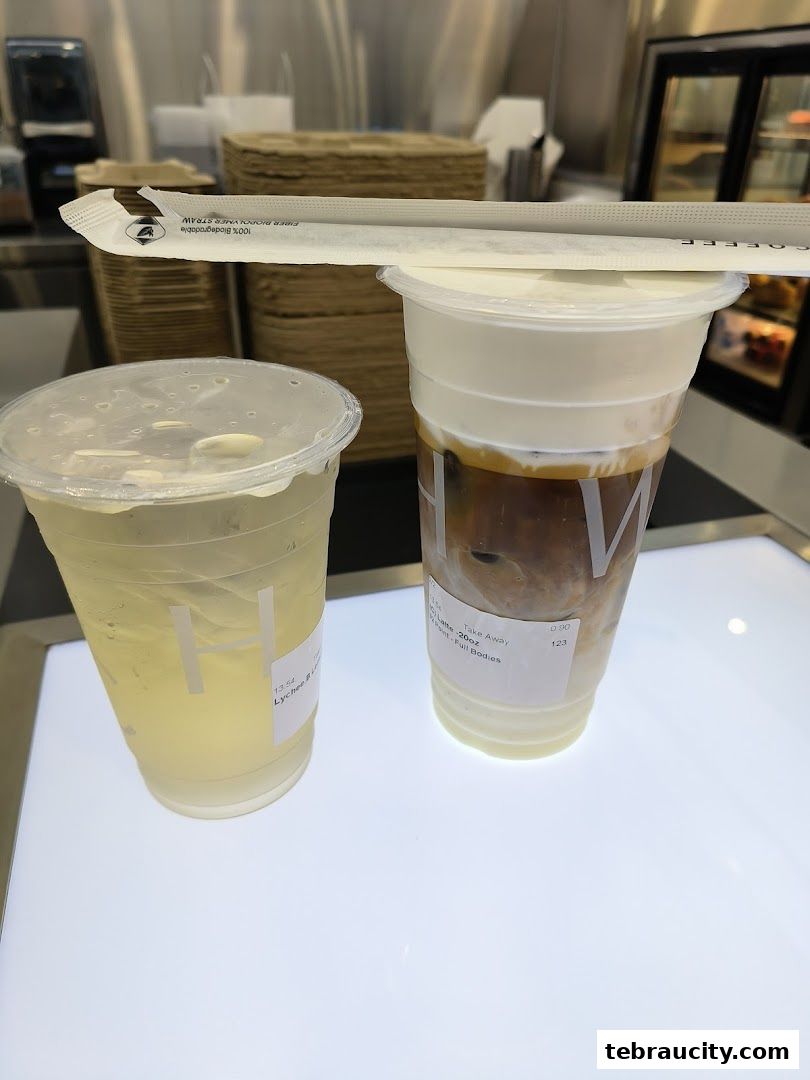 Two refreshing drinks, one a lychee beverage and the other a creamy latte, are displayed on a white surface.