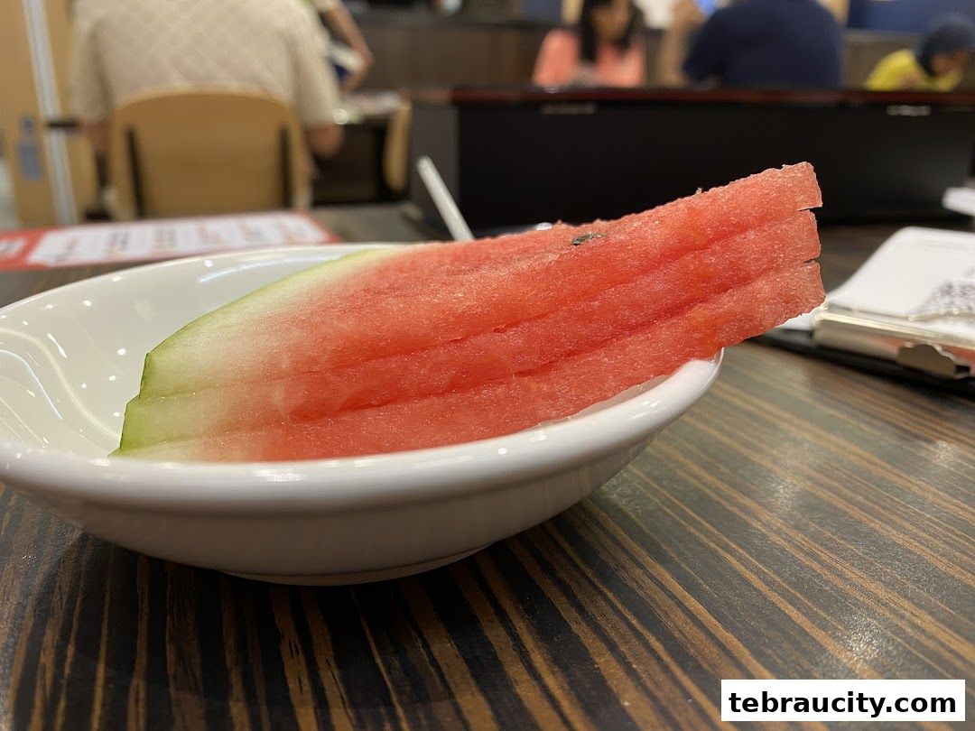 A close-up of sliced watermelon served in a white bowl on a wooden table.