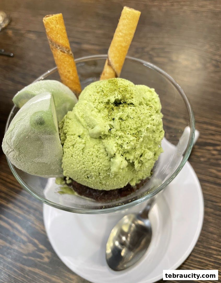 A refreshing matcha ice cream dessert with mochi and wafer sticks in a glass bowl.