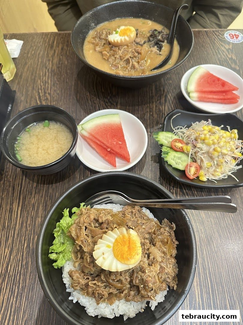 A table setting with two bowls of ramen, a side salad, miso soup, and watermelon slices.